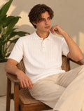 Model wearing a white cable knit short-sleeve polo with cream trousers