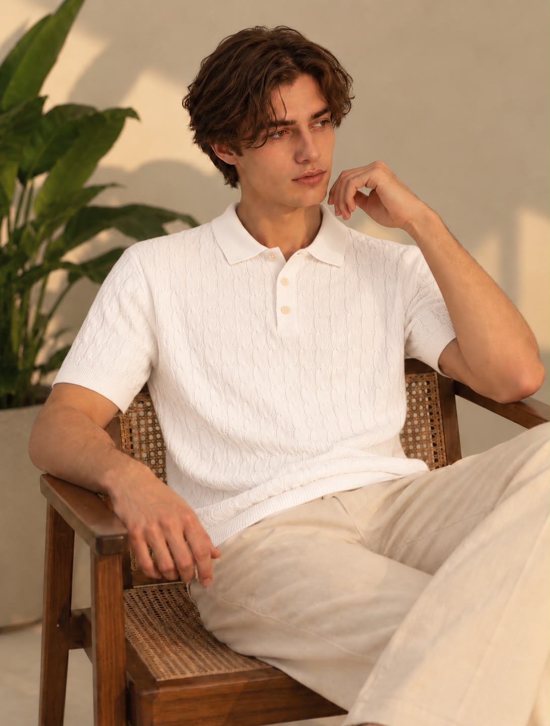 Model wearing a white cable knit short-sleeve polo with cream trousers