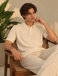 Model wearing BEZOKE cream cable knit short-sleeve polo with cream trousers